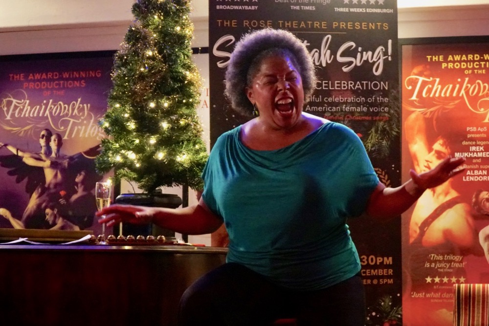 Andrea Baker sings beside piano and Christmas tree